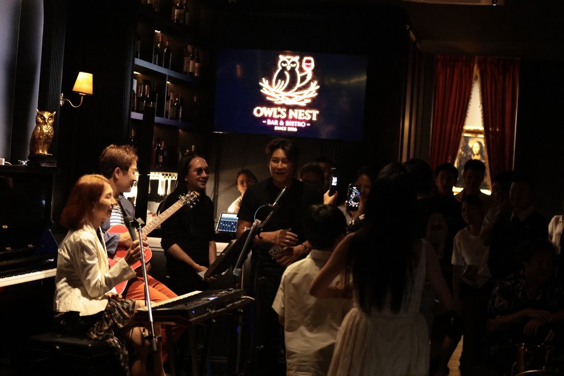 วงดนตรีสดเล่นหน้าป้ายนีออน Owl's Nest ในคืนวันหยุด